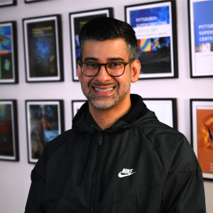 A man with medium-light skin tone and glasses smiles at the camera.