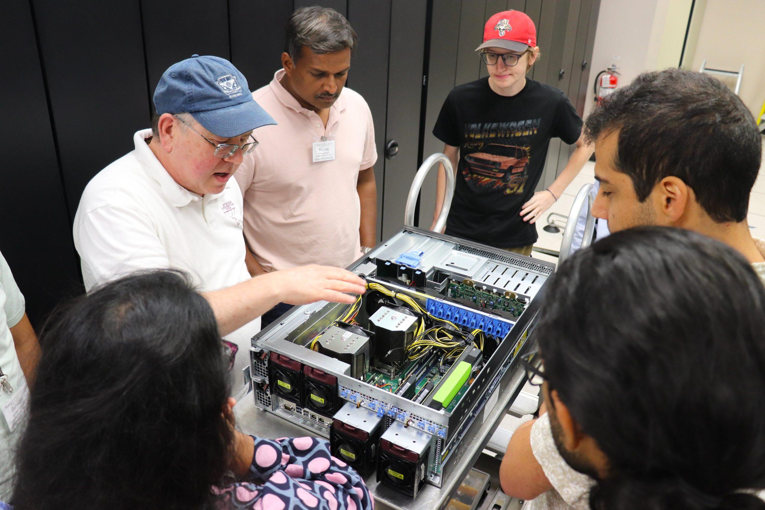 A group listens as a man describes the inside of a supercomputer component.