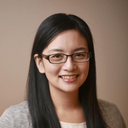 A woman with light skin tone and black hair smiles at the camera.