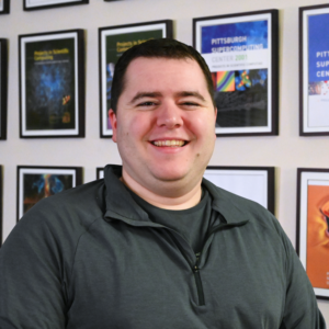 A man white light toned skin and brown hair smiles at the camera.